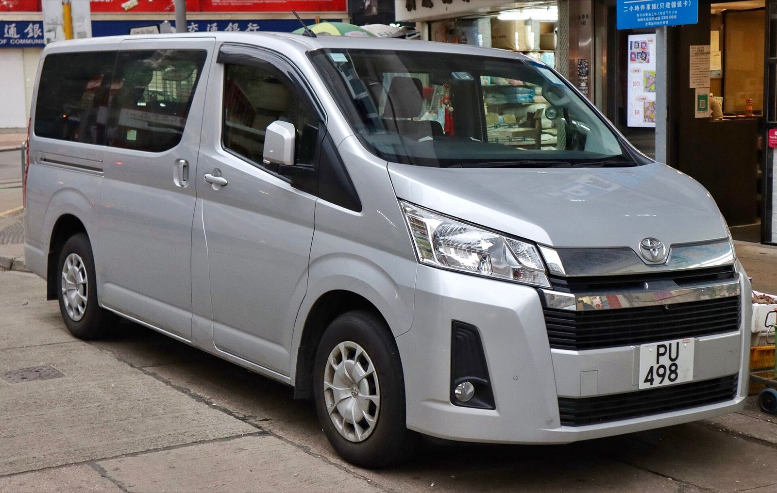 Silver Toyota HiAce passenger van parked on a city street, front three-quarter view