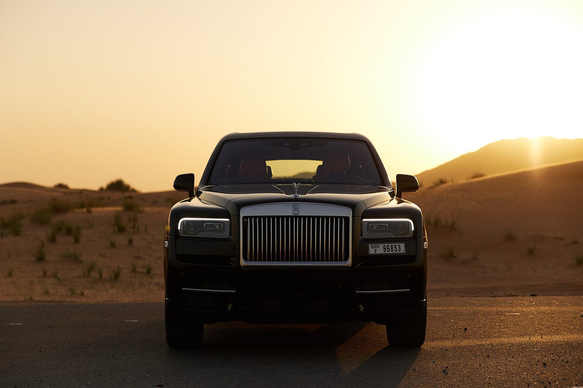 Black Rolls Royce Cullinan SUV with Dubai plates on a desert road at sunset