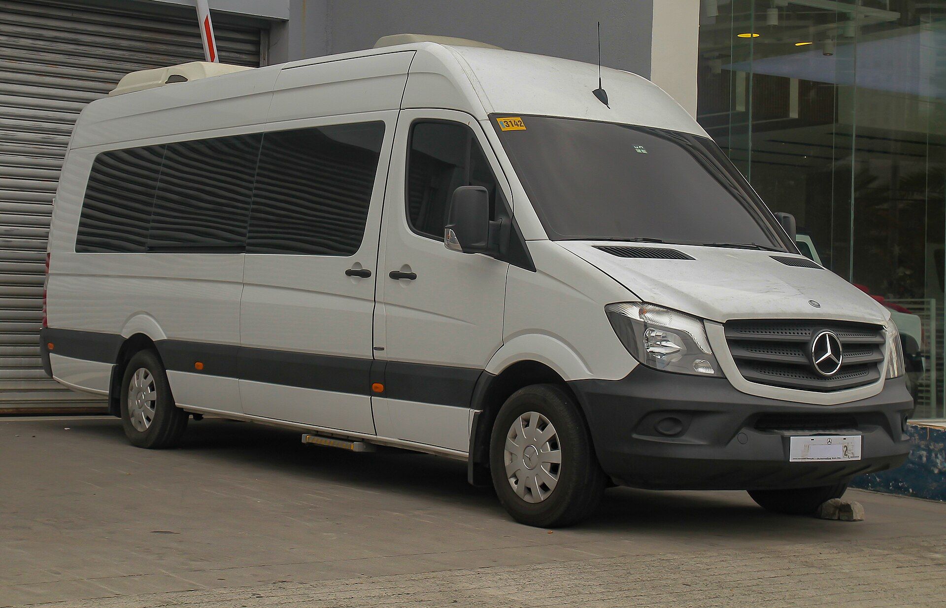 White Mercedes Benz Sprinter high roof passenger minibus parked by a building